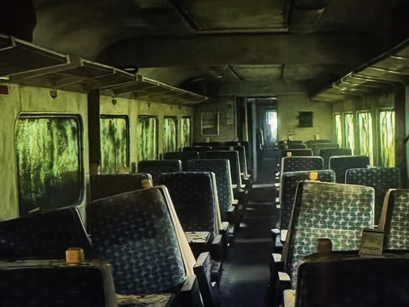 The moss-covered interior of an abandoned train carriage, rows of patterned seats under green light from overgrown windows