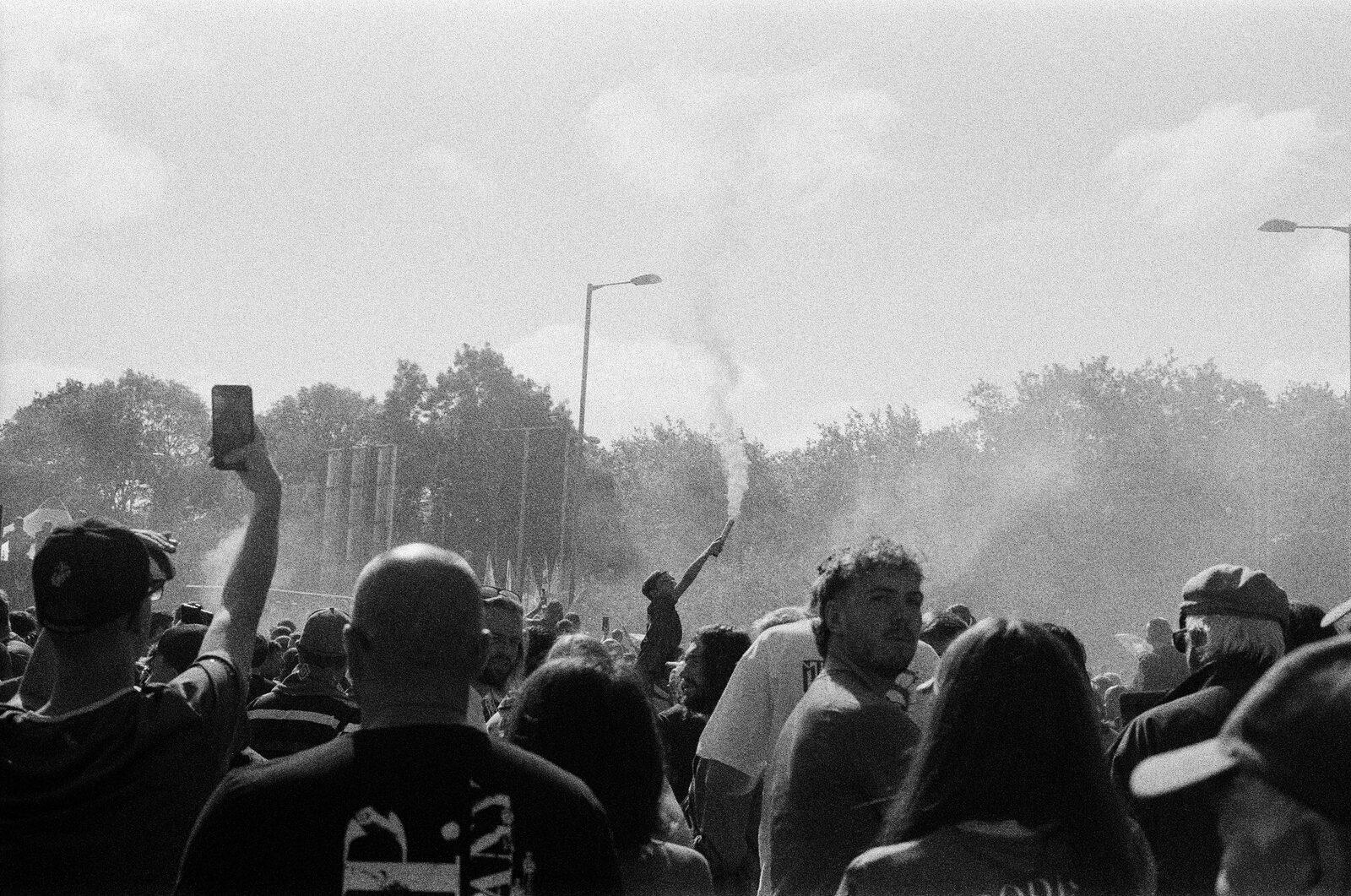 A fan holding a smoking flare aloft above a dense crowd, others raising phones to film