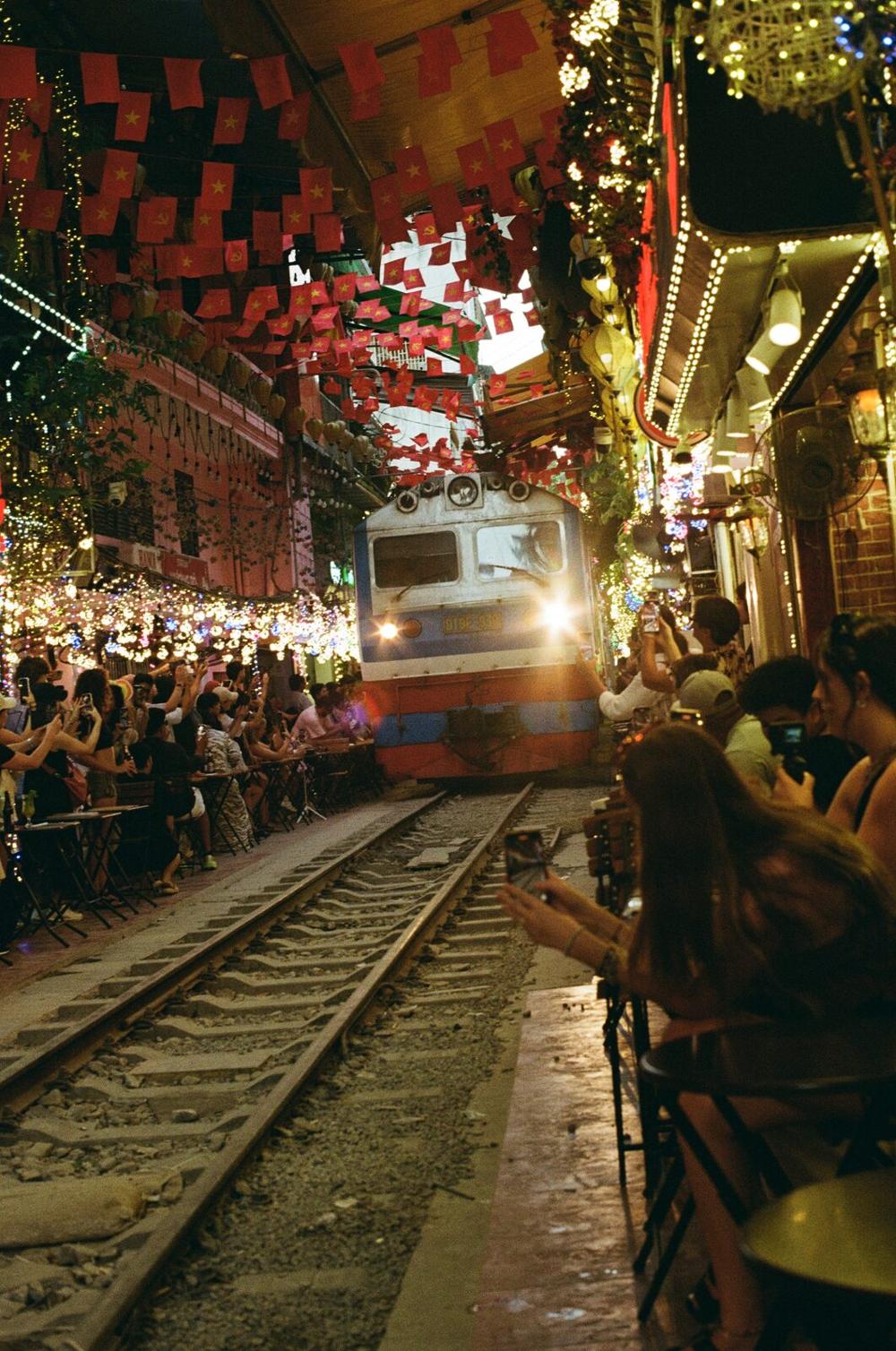 A train passing through the lantern-lit train street cafes of Hanoi at night